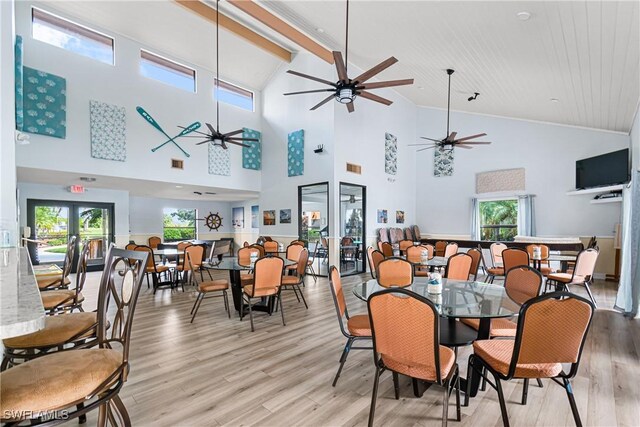 dining space with light hardwood / wood-style floors, beam ceiling, high vaulted ceiling, ceiling fan, and french doors