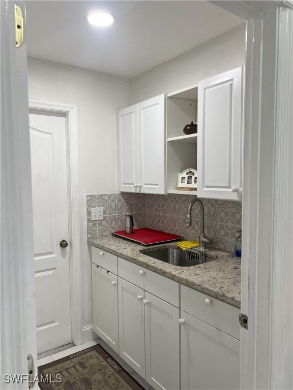 kitchen featuring light stone counters, white cabinetry, tasteful backsplash, and sink