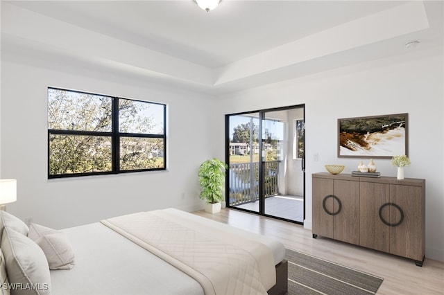 bedroom with a raised ceiling, access to exterior, and light wood-type flooring