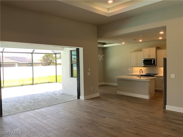 kitchen with tasteful backsplash, a kitchen island with sink, white cabinetry, hardwood / wood-style flooring, and refrigerator