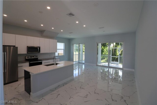 kitchen with backsplash, a kitchen island with sink, stainless steel appliances, sink, and white cabinetry