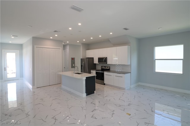 kitchen with white cabinets, backsplash, stainless steel appliances, sink, and a kitchen island with sink