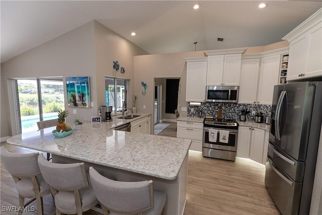 kitchen featuring white cabinets, a breakfast bar area, a sink, stainless steel appliances, and backsplash