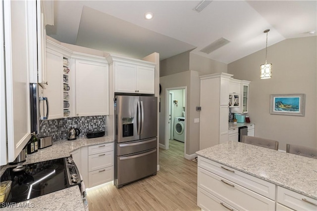 kitchen featuring vaulted ceiling, appliances with stainless steel finishes, washer / dryer, and white cabinetry