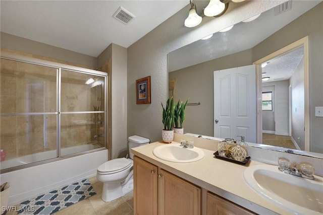 full bathroom featuring vanity, tile patterned floors, combined bath / shower with glass door, toilet, and a textured ceiling