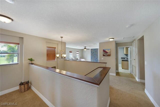 corridor featuring a notable chandelier, a textured ceiling, and light carpet