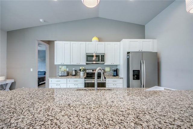 kitchen featuring light stone counters, appliances with stainless steel finishes, vaulted ceiling, white cabinetry, and a sink