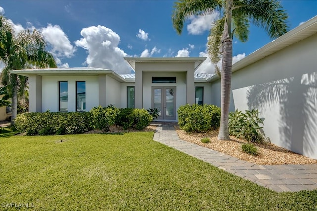 entrance to property with stucco siding, a lawn, and french doors