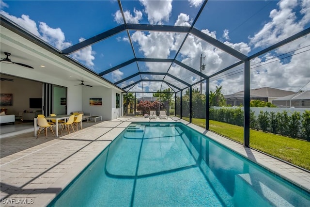 outdoor pool with glass enclosure, a lawn, a patio area, and a ceiling fan