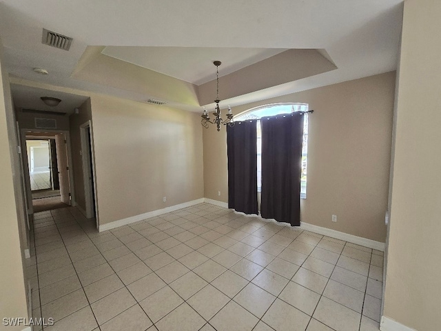 tiled spare room featuring a chandelier and a tray ceiling