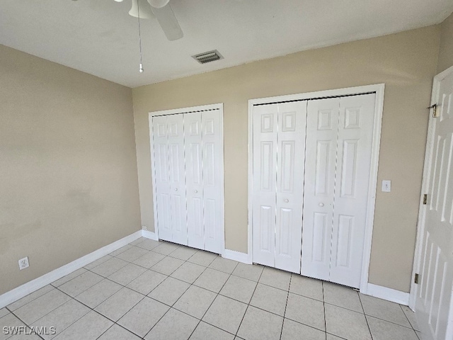 unfurnished bedroom featuring light tile patterned flooring, two closets, and ceiling fan