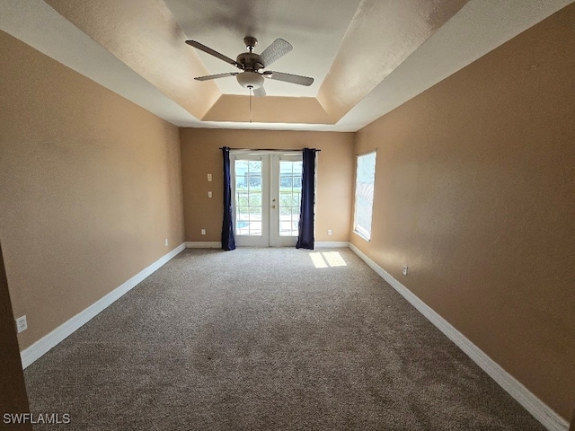 empty room with a raised ceiling, ceiling fan, french doors, and carpet flooring