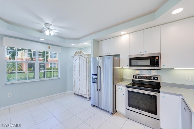 kitchen with stainless steel appliances, light tile patterned floors, ceiling fan, a raised ceiling, and white cabinets