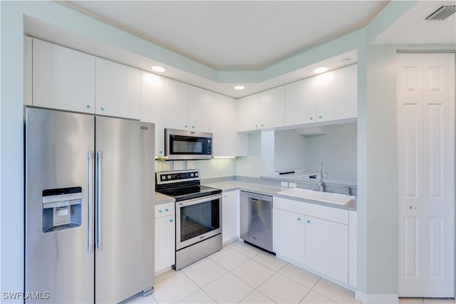 kitchen with stainless steel appliances, sink, light tile patterned floors, and white cabinetry