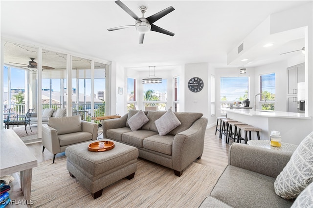 living room with light wood-type flooring, ceiling fan, a wealth of natural light, and a water view