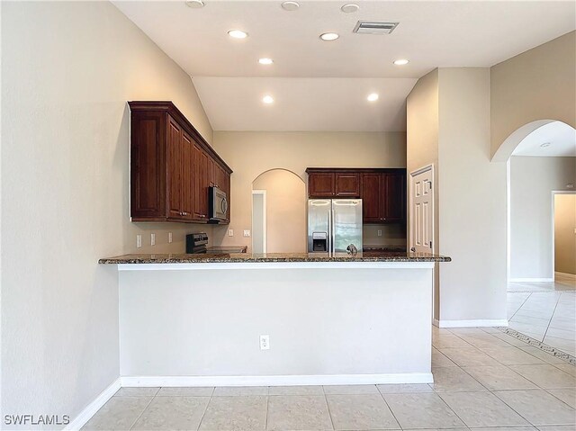 kitchen featuring appliances with stainless steel finishes, light tile patterned floors, dark stone counters, and kitchen peninsula