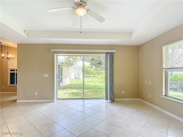 spare room with light tile patterned floors, ceiling fan with notable chandelier, and a tray ceiling