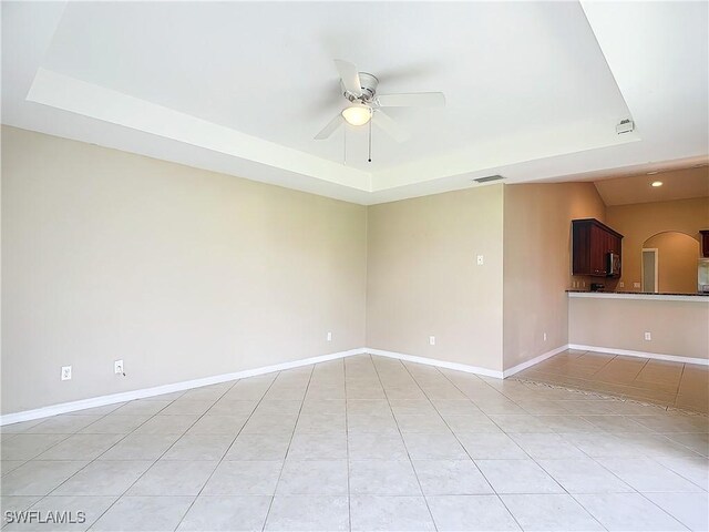 unfurnished room featuring a tray ceiling, ceiling fan, and light tile patterned flooring