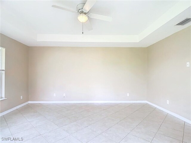 tiled empty room featuring a tray ceiling and ceiling fan