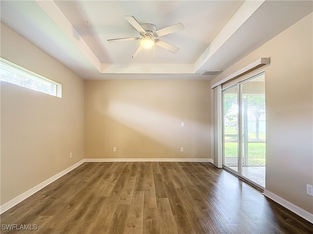 empty room featuring a tray ceiling, ceiling fan, and dark hardwood / wood-style floors