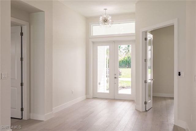 entryway with light wood-type flooring, french doors, a wealth of natural light, and an inviting chandelier