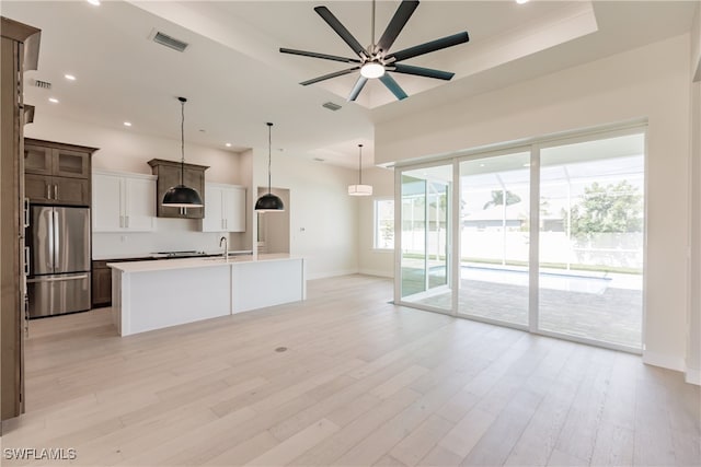 kitchen with stainless steel fridge, dark brown cabinets, a center island with sink, light hardwood / wood-style floors, and ceiling fan