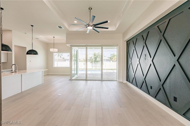 unfurnished living room featuring a tray ceiling, light wood finished floors, recessed lighting, ceiling fan, and a sink