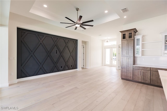 unfurnished living room with ceiling fan, a tray ceiling, and light hardwood / wood-style floors