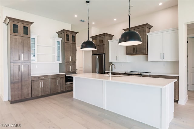 kitchen with white cabinets, light hardwood / wood-style flooring, stainless steel appliances, sink, and an island with sink