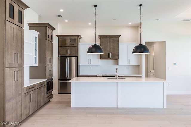 kitchen with a kitchen island with sink, light hardwood / wood-style flooring, stainless steel refrigerator, and hanging light fixtures