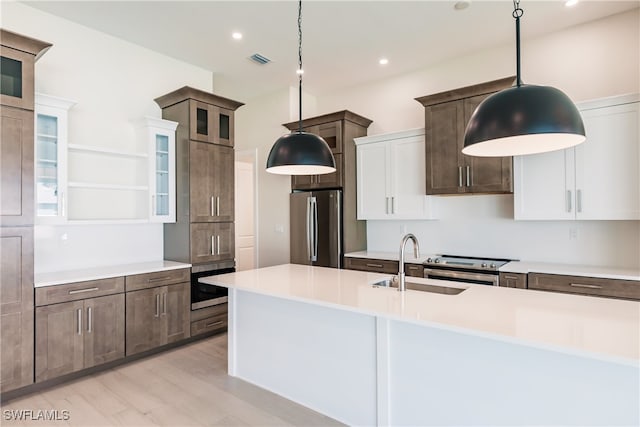 kitchen with light wood-type flooring, appliances with stainless steel finishes, white cabinetry, sink, and pendant lighting