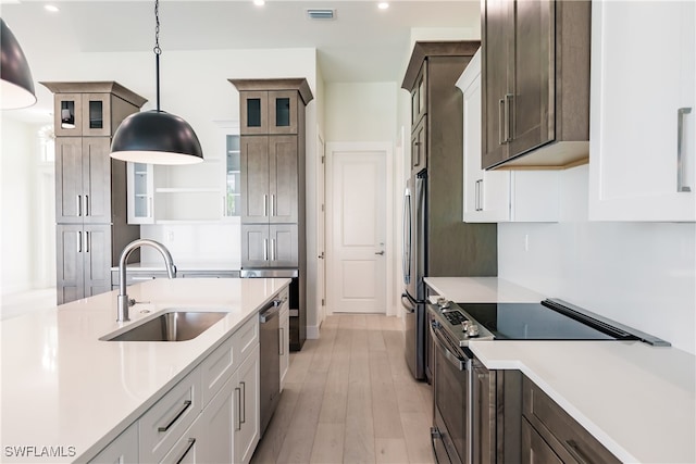 kitchen featuring pendant lighting, light hardwood / wood-style flooring, stainless steel appliances, sink, and white cabinets