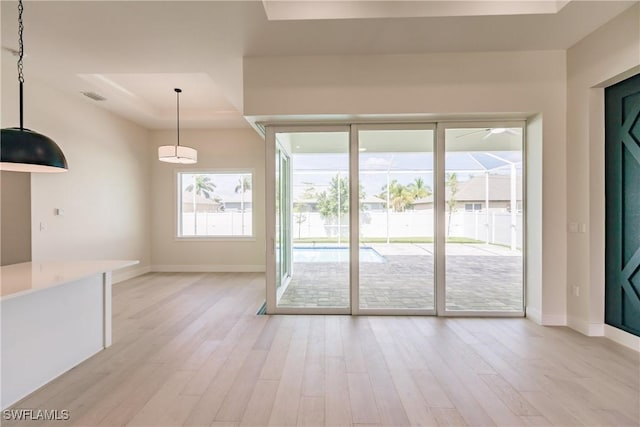 interior space with visible vents, a tray ceiling, light wood-style flooring, and baseboards