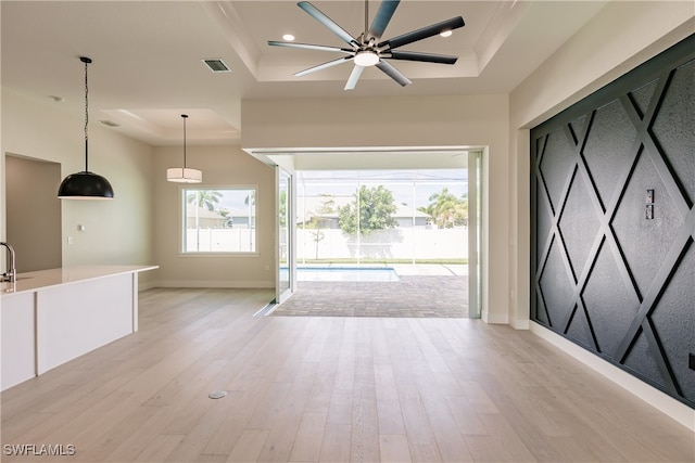 interior space with ceiling fan, a raised ceiling, and light hardwood / wood-style flooring