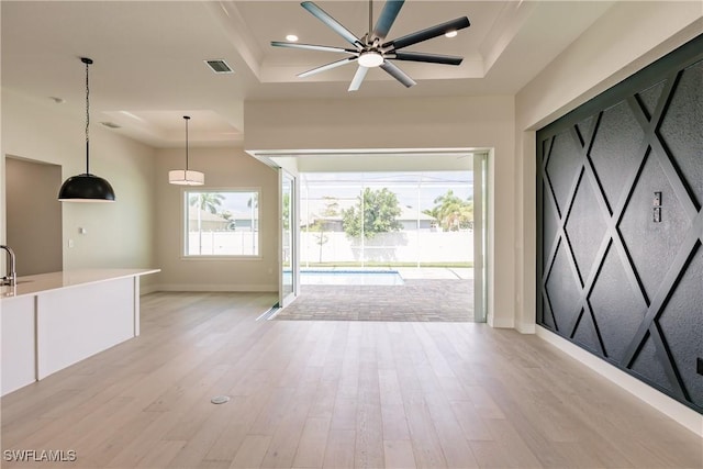 unfurnished living room featuring a raised ceiling, visible vents, light wood-style flooring, and baseboards