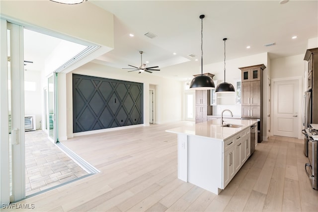 kitchen with light hardwood / wood-style flooring, a kitchen island with sink, hanging light fixtures, sink, and ceiling fan