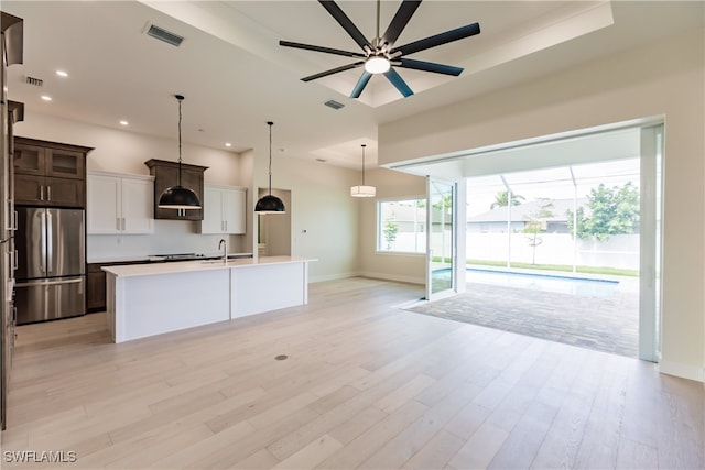 kitchen featuring light hardwood / wood-style flooring, stainless steel fridge, dark brown cabinets, ceiling fan, and a center island with sink