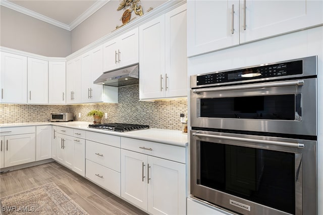 kitchen with stainless steel appliances, tasteful backsplash, crown molding, white cabinets, and light wood-type flooring