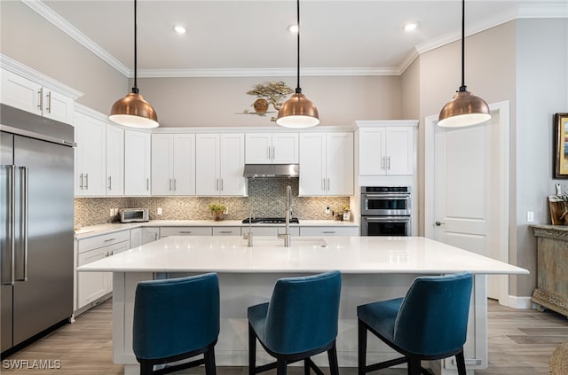 kitchen with appliances with stainless steel finishes, white cabinetry, pendant lighting, and a kitchen island with sink