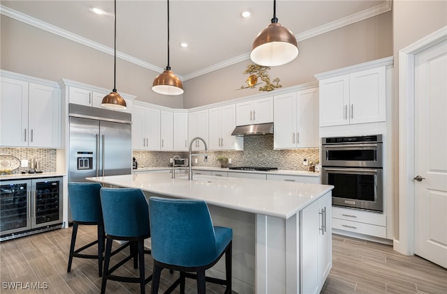 kitchen with sink, hanging light fixtures, wine cooler, white cabinets, and appliances with stainless steel finishes