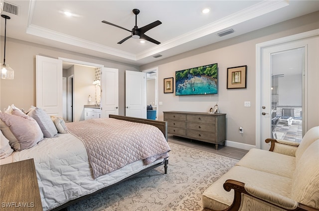 bedroom with ceiling fan, a raised ceiling, crown molding, ensuite bathroom, and light wood-type flooring