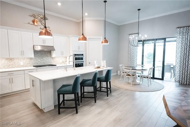 kitchen featuring appliances with stainless steel finishes, a towering ceiling, pendant lighting, white cabinetry, and a kitchen island with sink