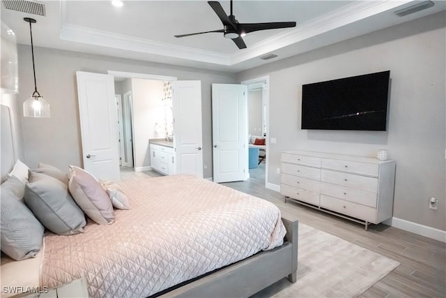 bedroom with light hardwood / wood-style floors, a tray ceiling, ornamental molding, ceiling fan, and ensuite bathroom