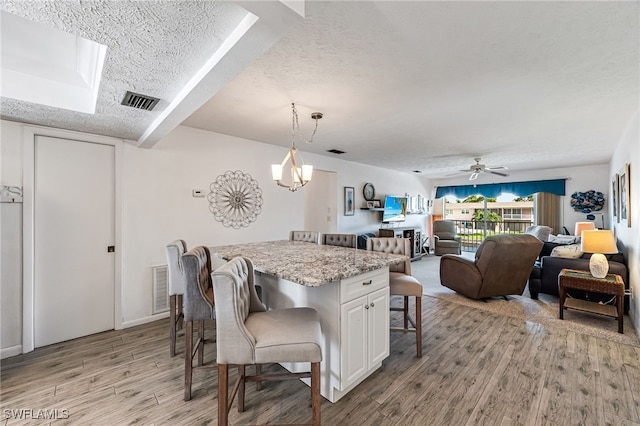 kitchen featuring white cabinets, light hardwood / wood-style flooring, ceiling fan with notable chandelier, a kitchen bar, and a textured ceiling