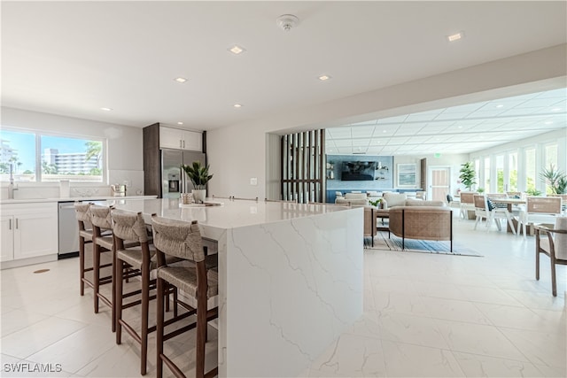 kitchen with a center island with sink, stainless steel appliances, light stone counters, white cabinets, and a kitchen bar