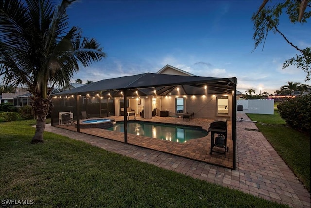 pool at dusk with an in ground hot tub, a patio area, and a lawn