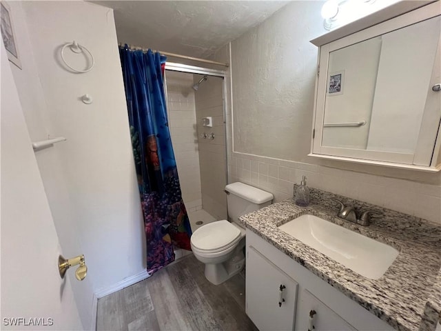 bathroom with vanity, hardwood / wood-style flooring, a shower with shower curtain, toilet, and tile walls