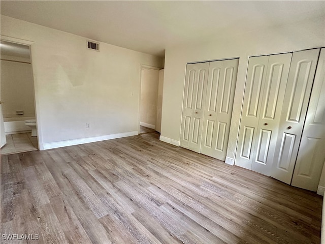 unfurnished bedroom featuring two closets, light wood-type flooring, and ensuite bath