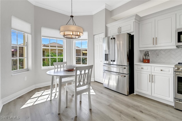 kitchen featuring pendant lighting, ornamental molding, white cabinetry, stainless steel appliances, and light hardwood / wood-style floors