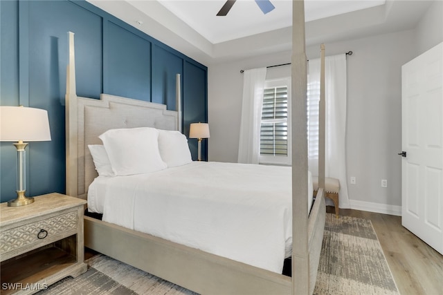 bedroom with ceiling fan, a raised ceiling, and light hardwood / wood-style floors